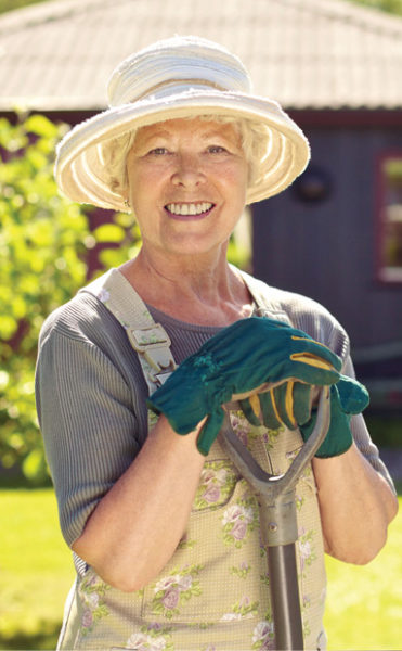 Cheerful elder woman gardening in backyard